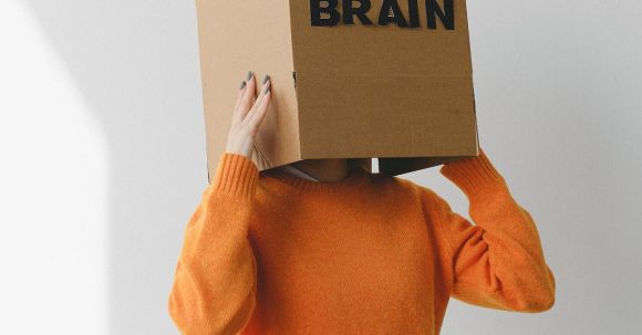 Finding Purpose - Crop person putting Idea title in cardboard box with Brain inscription on head of female on light background